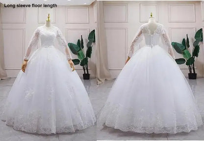 White wedding dress with long sleeves and floor length on mannequins against a light-colored wall.